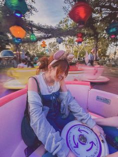 a woman sitting in the back of a pink boat at an amusement park with lanterns hanging from the ceiling