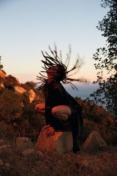 a woman with dreadlocks sitting on a rock