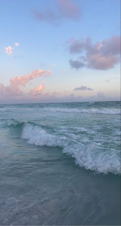 the waves are rolling in to the shore at sunset or dawn, with pink and blue clouds above