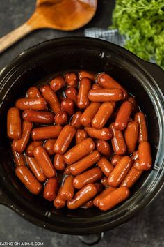 cooked hot dogs in a crock pot with wooden spoon and parsley on the side