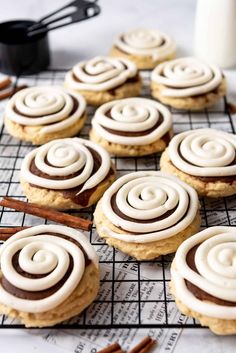 cinnamon roll cookies with white icing on a cooling rack next to some cinnamon sticks