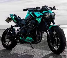 a green and black motorcycle parked on top of a road next to the ocean with clouds in the background