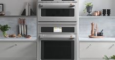 two ovens side by side in a kitchen with white counter tops and gray cabinets