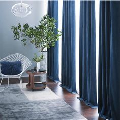 a living room with blue curtains and a white chair next to a potted plant