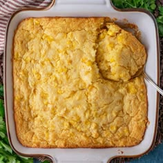 a square casserole dish with corn on top and a spoon in the middle