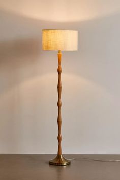 a wooden floor lamp with a white shade on the base and a beige fabric lampshade