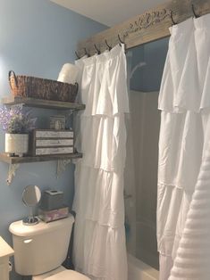 a white toilet sitting next to a bath tub in a bathroom under a wooden shelf