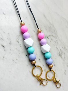 two necklaces on a marble surface with gold scissors and beads hanging from them,