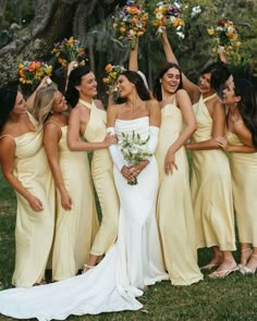 a group of women standing next to each other holding bouquets in their hands and wearing yellow dresses