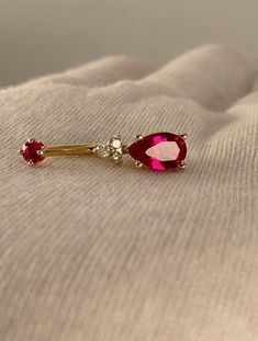 a pair of red and gold earrings sitting on top of a white cloth covered bed