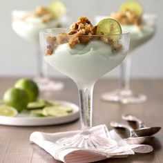 three glasses filled with dessert sitting on top of a wooden table next to silverware