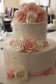 a three tiered cake with pink and white flowers on the top, sitting on a table