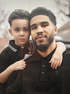 a man holding a little boy who is wearing a black shirt and has his arms around him