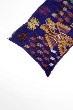 a blue pillow with colorful designs on the front and back, sitting on a white surface