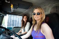 two women sitting in the driver's seat of a bus, one with sunglasses on