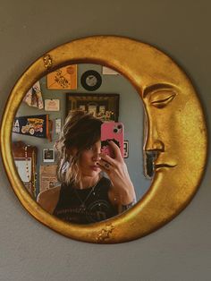 a woman taking a selfie in front of a mirror with a gold moon face on it