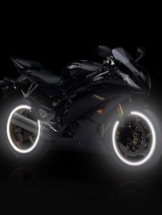 a black motorcycle parked in the dark with its lights on and it's wheels glowing