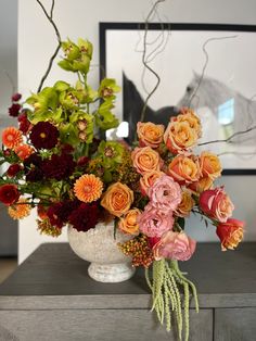 a white vase filled with lots of different colored flowers on top of a wooden table