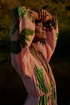 a woman in a pink dress is holding her hands up to her head and looking off into the distance