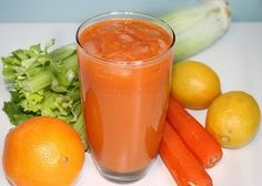 an orange juice in a glass surrounded by vegetables