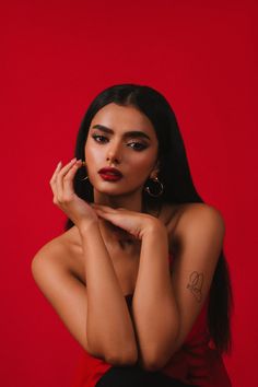 a woman with long black hair and red lipstick is posing for a photo in front of a red background