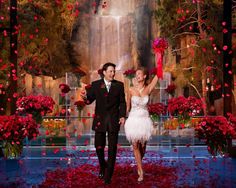 a man and woman dressed in tuxedos walking down a red carpet with rose petals