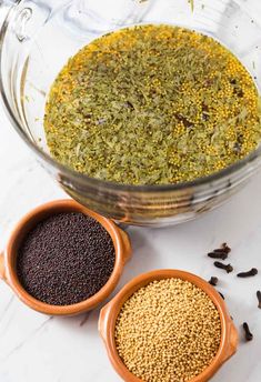 two bowls filled with spices next to each other on a white counter top, one containing seeds and the other containing seasonings