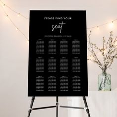 a black and white wedding seating chart on a tripod with lights in the background