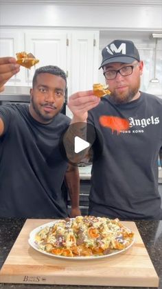 two men standing in front of a plate of food with one holding up a piece of bread