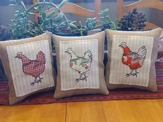 three pillows with chickens on them sitting on a table next to a potted plant