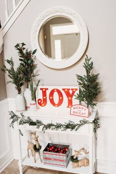 a white shelf with christmas decorations on it and a mirror hanging above the top that says joy