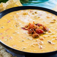 a black bowl filled with cheese and bacon dip surrounded by tortilla chips on the side