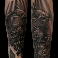 two dolphins on the arm with an ocean scene in black and grey ink, done by person