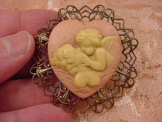 (Internal #CM69-1) Excellent, new, hand stained natural pine resin, hand-molded CHERUB ANGEL KISSING LADY IN CLOUDS HEART SHAPED CAMEO (reproduced from the original shell cameo)  pin/pendant in IVORY color with LIGHT PEACH color background, mounted on repro Victorian brass, 1-15/16" across x 1-15/16" long. Clasp pin/pendant glued on back. Superb detail. I know because I do half the work in creating the cameos. Comes with information card. WE SHIP WORLDWIDE! Other accepted payment: Credit card (M Vintage Peach Jewelry For Gifts, Antique Heart-shaped Brooch For Gift, Antique Heart-shaped Brooches As Gifts, Antique Heart-shaped Brooches For Gifts, Peach Color Background, Angel Cherub, Light Peach Color, Cherub Angel, Brass Pin