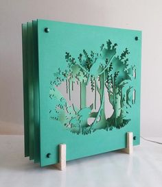 a green box with cut out trees on the front and sides, sitting on top of a white table