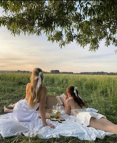 two women are sitting on the grass eating and drinking