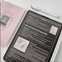 an electronic device sitting on top of a table next to a pink notebook and pen