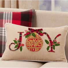 a christmas ornament pillow on a couch in front of a window with plaid curtains