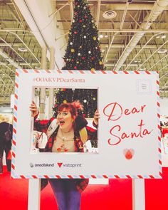 a woman standing in front of a christmas tree holding up a sign that says dear santa