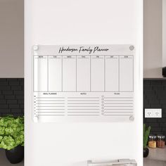 a dry erase board mounted to the side of a kitchen wall next to a potted plant