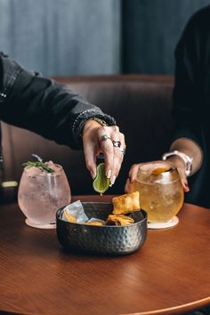 two people sitting at a table with drinks and food in front of them, one holding a lime