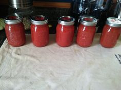 four jars filled with red liquid sitting on top of a counter