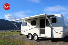 an rv parked on the side of a dirt road near a body of water with mountains in the background