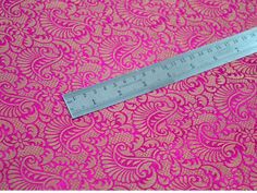 a ruler is on top of a pink and gold brocade print fabric that has been cut in half