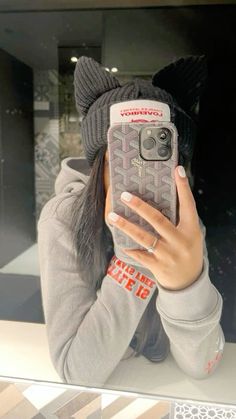 a woman taking a selfie in front of a mirror wearing a hat and sweater