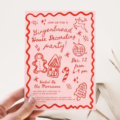 a hand holding up a pink card with gingerbread house decorating party on it