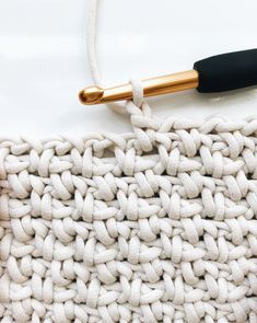 two hands crocheting together on a knitted blanket with a gold colored needle