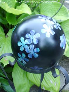 a black ball with blue flowers painted on it sitting in front of some green leaves