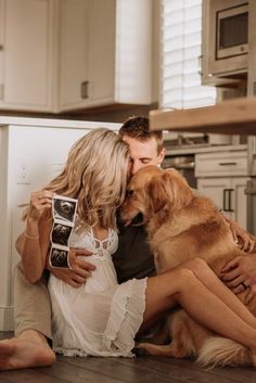 a man and woman kissing while sitting on the floor with a dog in front of them