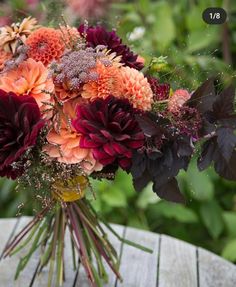 a bouquet of flowers sitting on top of a wooden table in front of some bushes